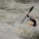 A whitewater kayaker paddles through a large rapid while water crashes over the bow of the kayak.