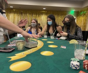 Three Westminster students in black tie attire sit at a Blackjack table at ASW Casino Night as the dealer reaches for cards.