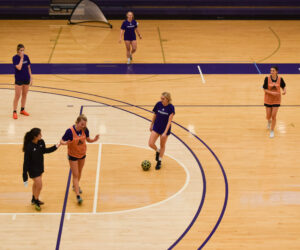 Griffin women’s soccer team players pause and talk during their off-season practice on a basketball court.