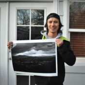 A male student holds up an image, standing in front of a building.