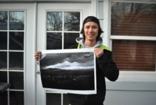 A male student holds up an image, standing in front of a building.