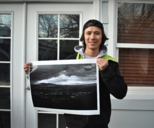 A male student holds up an image, standing in front of a building.