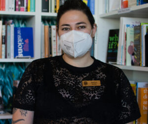 Kaitlyn Mahone, the owner of Under the Umbrella, a queer bookstore, stands in front of their favorite section in the store, the nonfiction section on Feb. 26.