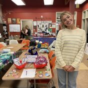 A woman in a gray and beige sweater stands in front of a table decorated with candy and brightly colored decorations.