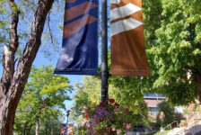 Two Westminster College banners, copper and dark purple, and a flower basket hang from a light post in Richer Commons.