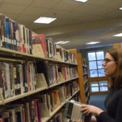 A woman stands and stacks books in a hallway of shelved books