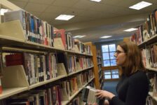 A woman stands and stacks books in a hallway of shelved books