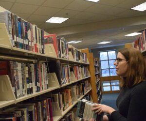 A woman stands and stacks books in a hallway of shelved books