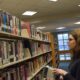 A woman stands and stacks books in a hallway of shelved books