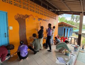Nine Westminster students paint an image of a tree and a snake on the wall at a school in Thailand.