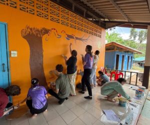 Nine Westminster students paint an image of a tree and a snake on the wall at a school in Thailand.