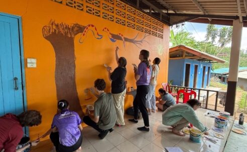 Nine Westminster students paint an image of a tree and a snake on the wall at a school in Thailand.