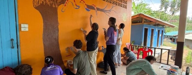 Nine Westminster students paint an image of a tree and a snake on the wall at a school in Thailand.