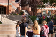 President Beth Dobkin stands behind a lectern on the stairs in front of Converse Hall while contributors to this partnership stand beside her to the right.