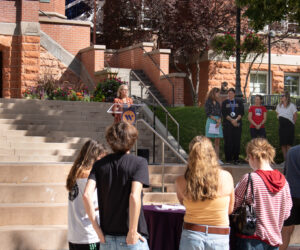 President Beth Dobkin stands behind a lectern on the stairs in front of Converse Hall while contributors to this partnership stand beside her to the right.
